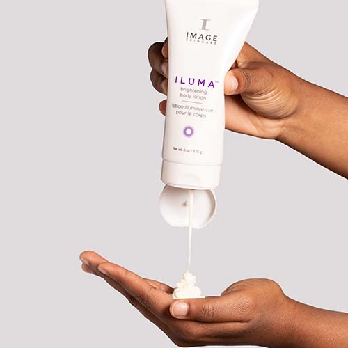 Een model knijpt in de witte tube van de Image Skincare Iluma Intense Brightening Body Lotion, waarbij de romige witte lotion in de handpalm wordt aangebracht.
