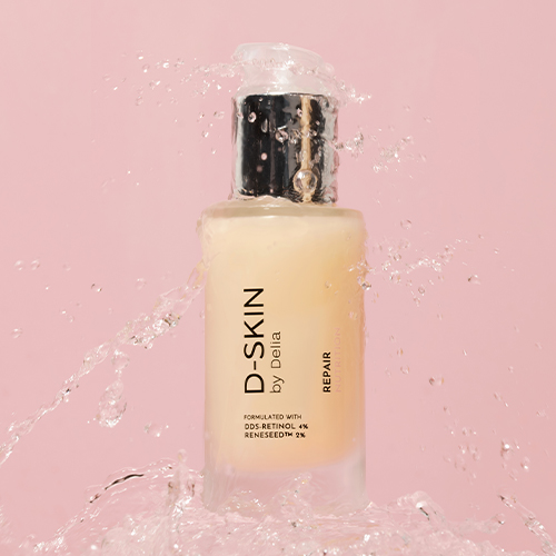 Een flacon D-SKIN Repair Nutrition serum omringd door opspattend water tegen een roze achtergrond.