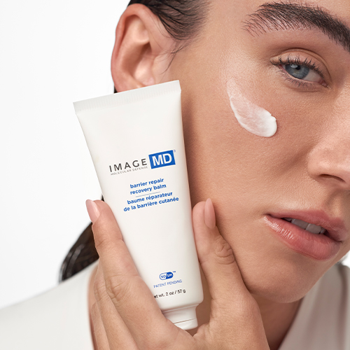Close-up van een vrouw die de IMAGE Skincare IMAGE MD recovery balm op haar wang heeft aangebracht, terwijl ze de tube vasthoudt.