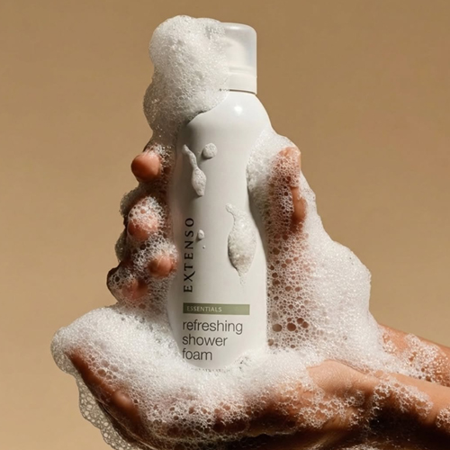 Een hand die een fles Extenso Refreshing Shower Foam vasthoudt, omhuld met een royale hoeveelheid doucheschuim.