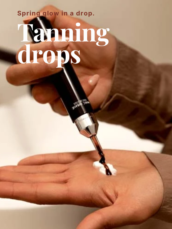 Close-up van handen die Marc Inbane tanning drops toevoegen aan een toefje witte crème in een handpalm, met de Engelse tekst 'Spring glow in a drop'.