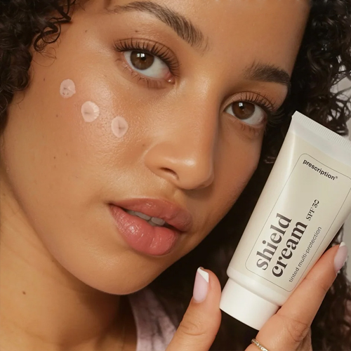 Model met druppels crème op haar wang en een tube prescription shield cream spf30 in haar hand