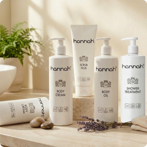 De hannah body lijn met 4 grote verpakkingen langs elkaar. beige achtergrond de body scrub staat op een verhoging en voor de body oil licht een takje lavendel