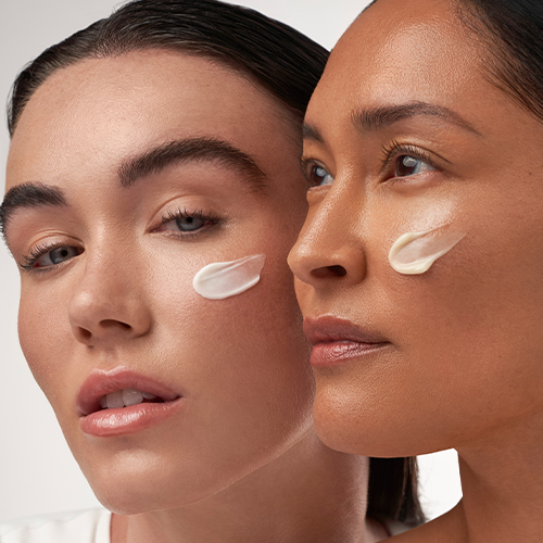 Twee vrouwen van dichtbij gefotografeerd met een kleine hoeveelheid witte gezichtscrème op hun jukbeenderen om de textuur van de IMAGE MD producten te tonen.