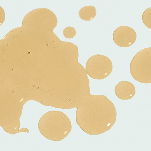 Close-up van de vloeibare, goudgele textuur en druppels van het Iluma Intense Facial Illuminator serum.