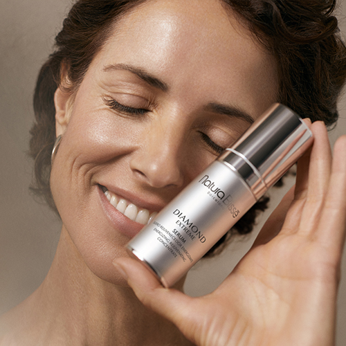 Een close-up van een model met een stralende huid tegen een kleurrijke paars-roze achtergrond, passend bij de luxe uitstraling van Natura Bissé.