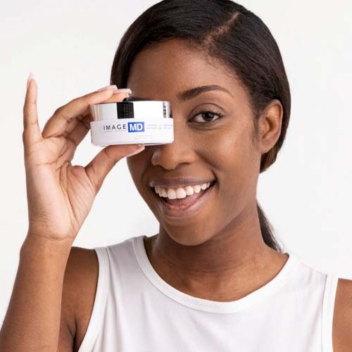 Lachende vrouw die de pot IMAGE MD Restoring Eye Masks bij haar gezicht houdt.