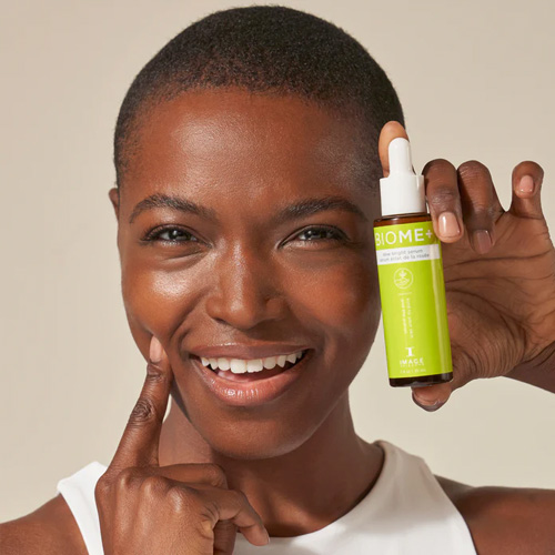 Een persoon brengt druppels van het BIOME+ Dew Bright Serum aan op de jukbeenderen voor een natuurlijke glow en hydratatie.