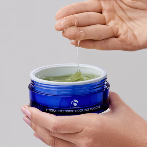Handen die de blauwe pot van iS Clinical Hydra-Intensive Cooling Masque vasthouden, terwijl vingers een hoeveelheid van de stroperige, transparant groene gelmasker textuur omhoog trekken