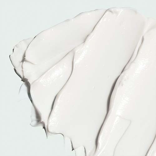 Een close-up van de rijke, witte crème-textuur van de Iluma Intense Brightening Eye Crème met zachte uitsmeringen.