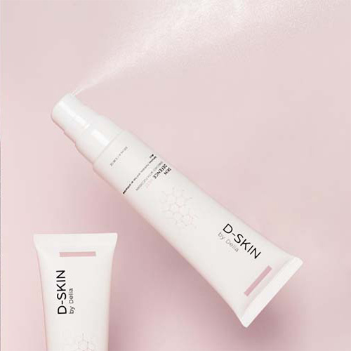 Een flesje D SKIN Skin Defence Mist dat een nevel sprayt, schuin geplaatst op een roze achtergrond