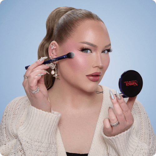 NikkieTutorials brengt blush aan op haar jukbeenderen met een kwast en houdt een Nimya poederdoosje vast voor een dagelijkse make-up look.