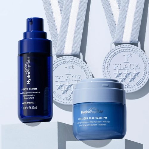 Een sfeervolle opstelling van HydroPeptide Power Serum en Collagen Reactivate PM op witte blokken met twee zilveren '1st Place' medailles op de achtergrond.