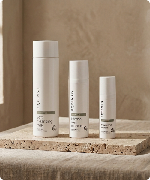 Drie witte flessen van de Extenso Essentials lijn, bestaande uit soft cleansing milk, intense skin moisture en hyalurenic serum, opgesteld op een natuurstenen plateau.