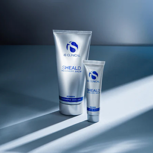 Twee zilveren tubes van iS Clinical Sheald Recovery Balm in groot en klein formaat met schaduwen op een blauwgrijze achtergrond