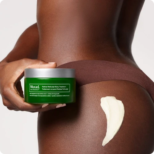 Een close-up foto van een hand die een pot Murad ReSculpt Body Treatment vasthoudt tegen de heup van een model, met een swatch van de crème-textuur op de huid.