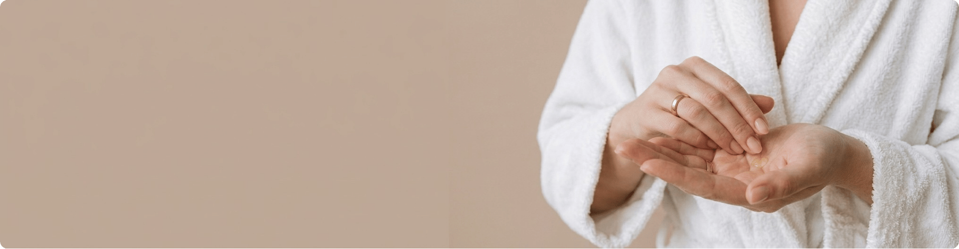 Een brede banner van iemand in een witte badjas die een hannah product in de handpalm aanbrengt tegen een beige achtergrond.