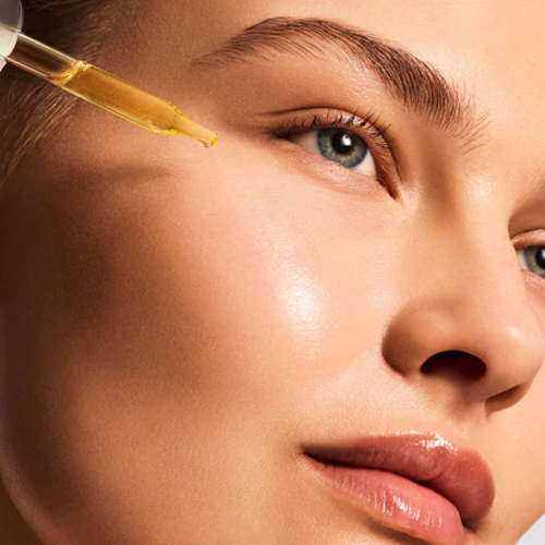 Close-up van een model waarbij een gouden serum met een pipet op de wang wordt aangebracht