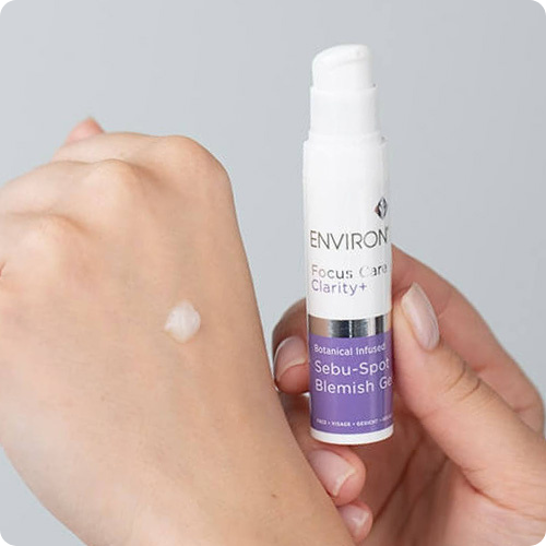 Een hand houdt het flaconnetje Environ Focus Care Clarity+ Sebu-Spot Blemish Gel vast, met een druppel gel op de rug van de andere hand