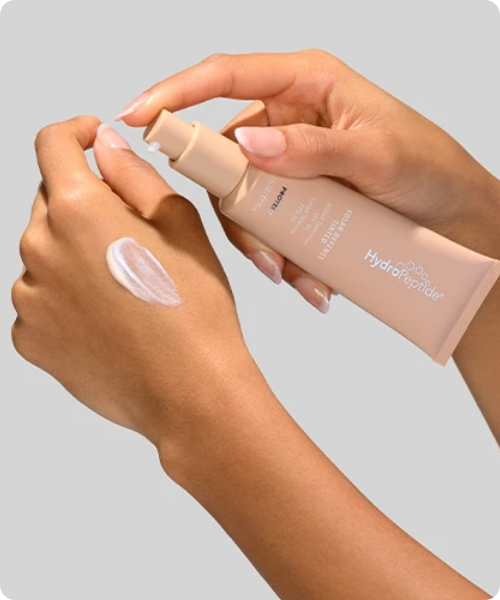 Handen die een tube HydroPeptide Solar Defense Tinted SPF 30 vasthouden en een dosering crème op de handrug aanbrengen