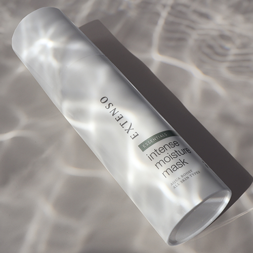 Sfeerfoto van de flacon Extenso Intense Moisture Mask (150ml) liggend in water, met reflecties en lichtinval op de verpakking.