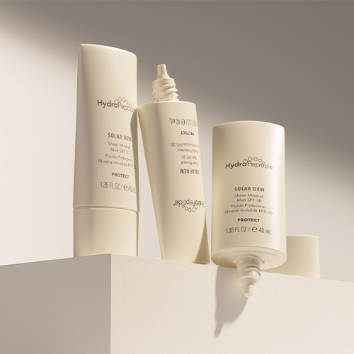 Drie tubes HydroPeptide Solar Dew Sheer Mineral Melt SPF 30 op een witte podiumopstelling