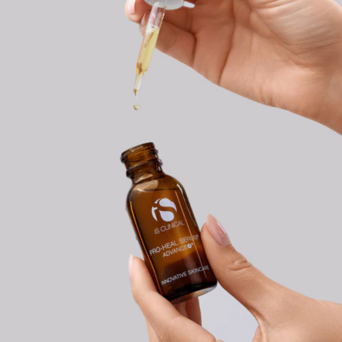 Hand die een gouden serum met een pipet uit het amberkleurige flesje van iS Clinical Pro-Heal Serum Advance+ in de handpalm laat druppelen