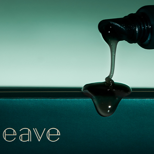 Een gedetailleerde opname van een dikke, glanzende druppel lipcare die uit een donkergroene tube op een oppervlak vloeit.