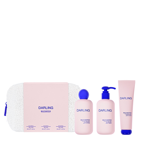 Een productfoto op een witte achtergrond van de Darling Multi Biotics set. De set bestaat uit een witte, pluizige toilettas en drie lichtroze flessen en een tube met blauwe doppen voor lichaamsproducten.