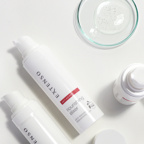 Platgelegd sfeerbeeld met meerdere Extenso nourishing elixer flacons en een glazen schaaltje met een transparante vloeistof