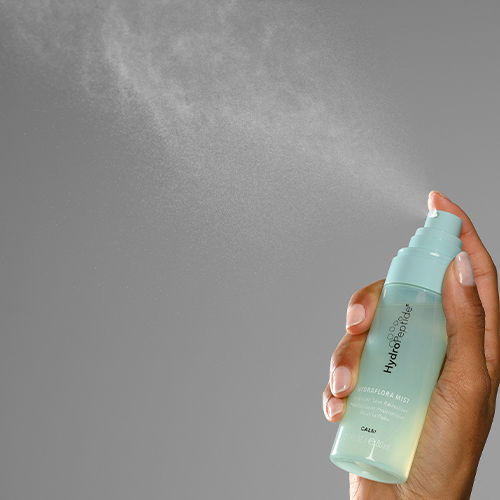Hand die een HydroPeptide HydraFlora Mist flacon vasthoudt tijdens het sprayen