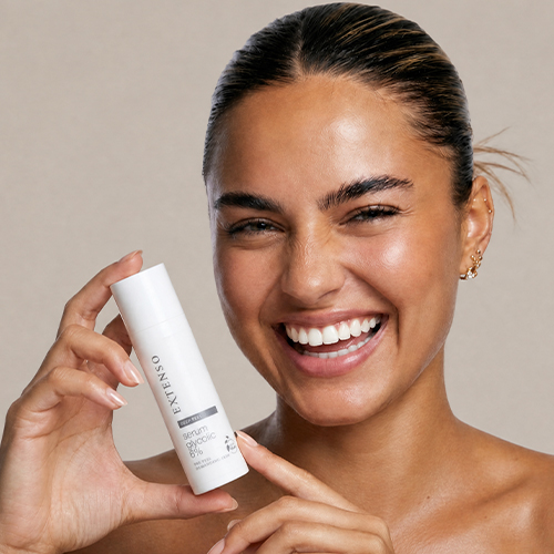Een vrolijke vrouw die een flesje Extenso Serum Glycolic 8% vasthoudt en naar de camera glimlacht.