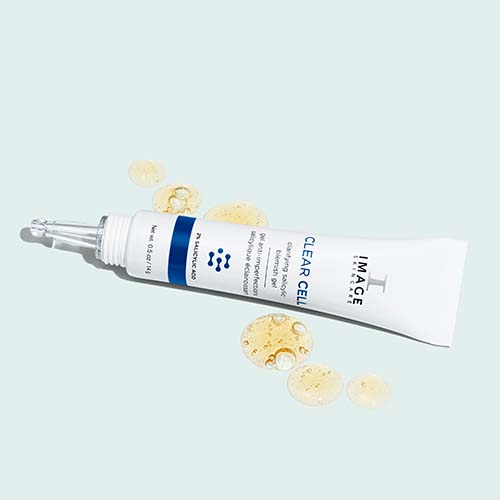 De tube van de Clear Cell Blemish Gel liggend tussen vloeibare druppels van de goudkleurige gel.