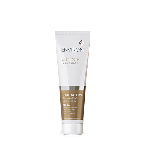Een staande witte tube Environ Rad Activé Antioxidant Sun Cream SPF 20 uit de Even More Sun Care+ lijn. De tube heeft bronskleurige accenten en vermeldt dat het product zweetbestendig is en breedspectrum UVA- en UVB-bescherming biedt.