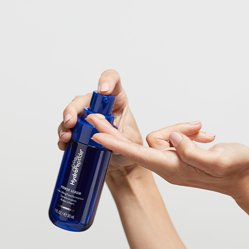 Iemand pompt een hoeveelheid HydroPeptide Power Serum op de vingertop vanaf een blauwe flacon van 30 ml.