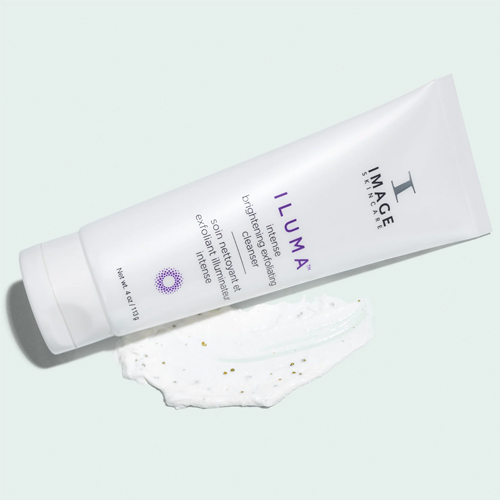De witte tube van de Image Skincare Iluma Intense Brightening Exfoliating Cleanser ligt horizontaal op een decoratieve uitsmering van het product.