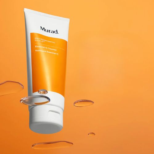 Murad Essential C Cleanser tube op een oranje achtergrond met waterdruppels