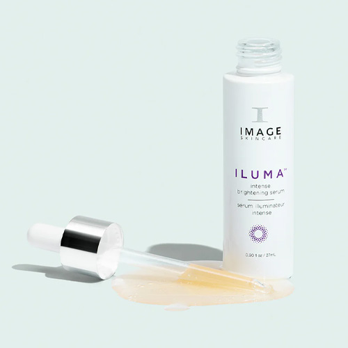 Een geopende flacon van het Image Skincare Iluma Intense Brightening Serum met een pipet die in een plasje goudkleurig serum ligt op een lichtblauwe achtergrond.