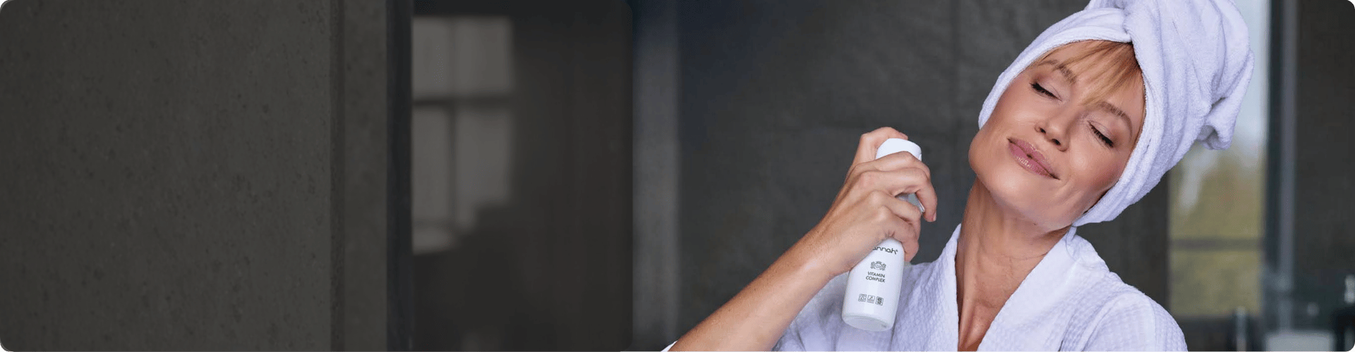 Vrouw met een witte handdoek om haar haar die hannah Vitamin Complex spray over haar hals en gezicht vernevelt