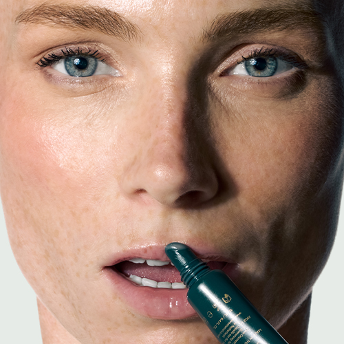 Close-up van een model met sproetjes dat de transparante Eave I AM GLAM Peptide Lip Care rechtstreeks op de lippen aanbrengt.