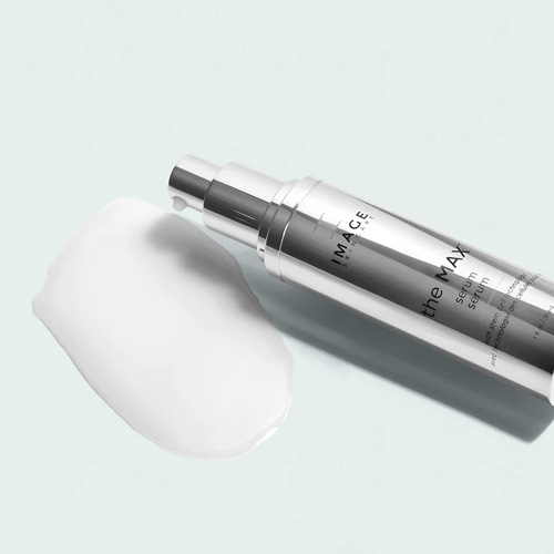 Het zilveren the MAX serum flesje liggend naast een druppel vloeibaar serum.
