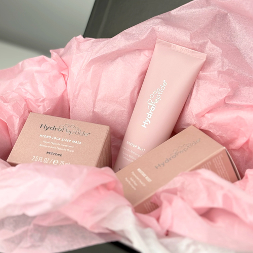De roze producten en doosjes van de HydroPeptide Care With Love set verpakt in feestelijk roze vloeipapier.