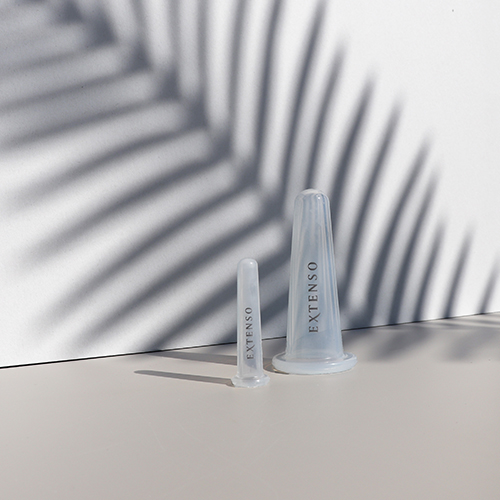 Twee transparante Extenso gezichtscups voor cupping massage op een lichte ondergrond met een schaduw van een palmblad