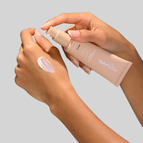 Hand drukt zonnebrandcrème uit een getinte HydroPeptide Solar Defense tube op de handrug