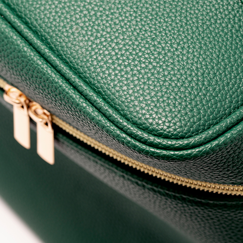 Close-up van de Eave vanity bag die de fijne korrelstructuur van het groene leer en de dubbele goudkleurige metalen ritstrekkers laat zien.