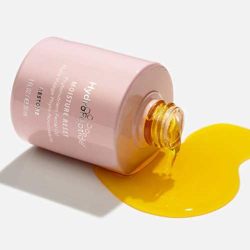 Een liggend roze flesje HydroPeptide Moisture Reset gezichtsolie waar heldere gele olie uit drukt op een witte achtergrond.