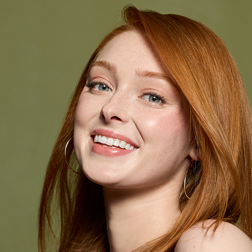 Lachend roodharig model met subtiele oogmake-up op een groene achtergrond