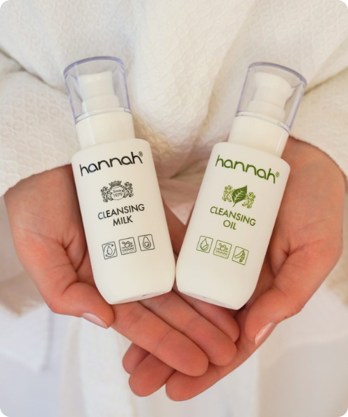 Iemand houdt de hannah Cleansing Milk en hannah Cleansing Oil in de handen tegen een witte achtergrond