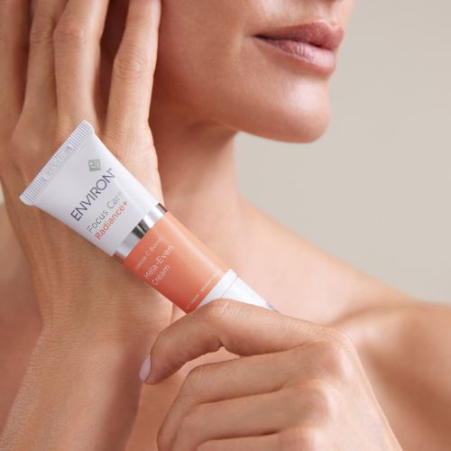 Sfeerbeeld van een model die de Environ Focus Care Radiance+ Intense C-Boost Mela-Even Cream tube vasthoudt bij haar gezicht.