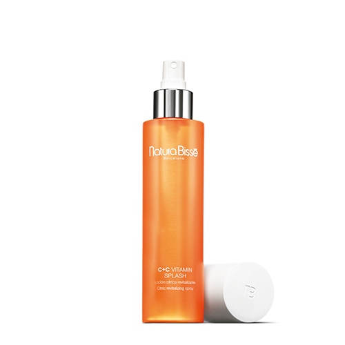 De oranje fles Natura Bissé C+C Vitamin Splash zonder dop, waarbij de zilveren sprayverstuiver zichtbaar is.
